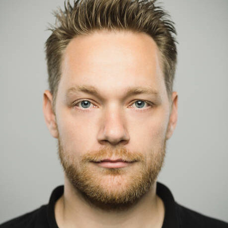 Close up portrait of young adult scandinavian man with blank expression against gray background. Vertical shot of real caucasian man staring in studio with blond hair and modern haircut. Photography from a DSLR camera. Sharp focus on eyes.